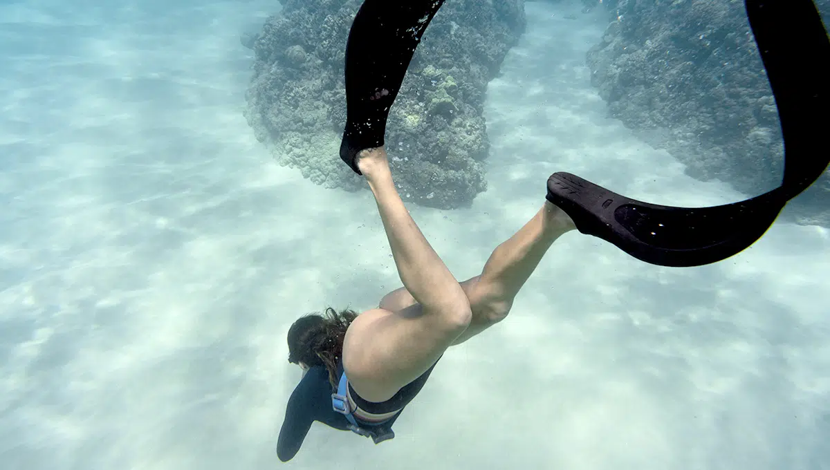 Femme en apnée sous l'eau, nageant près du fond marin avec des palmes noires